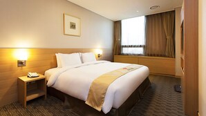 A hotel room with a neatly made bed, a bedside lamp, a small nightstand with a phone, a framed picture on the wall, and a window with curtains.