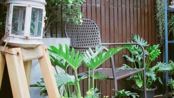 Una terraza de madera con un farol, sillas, plantas en macetas y una pared con formas geométricas.