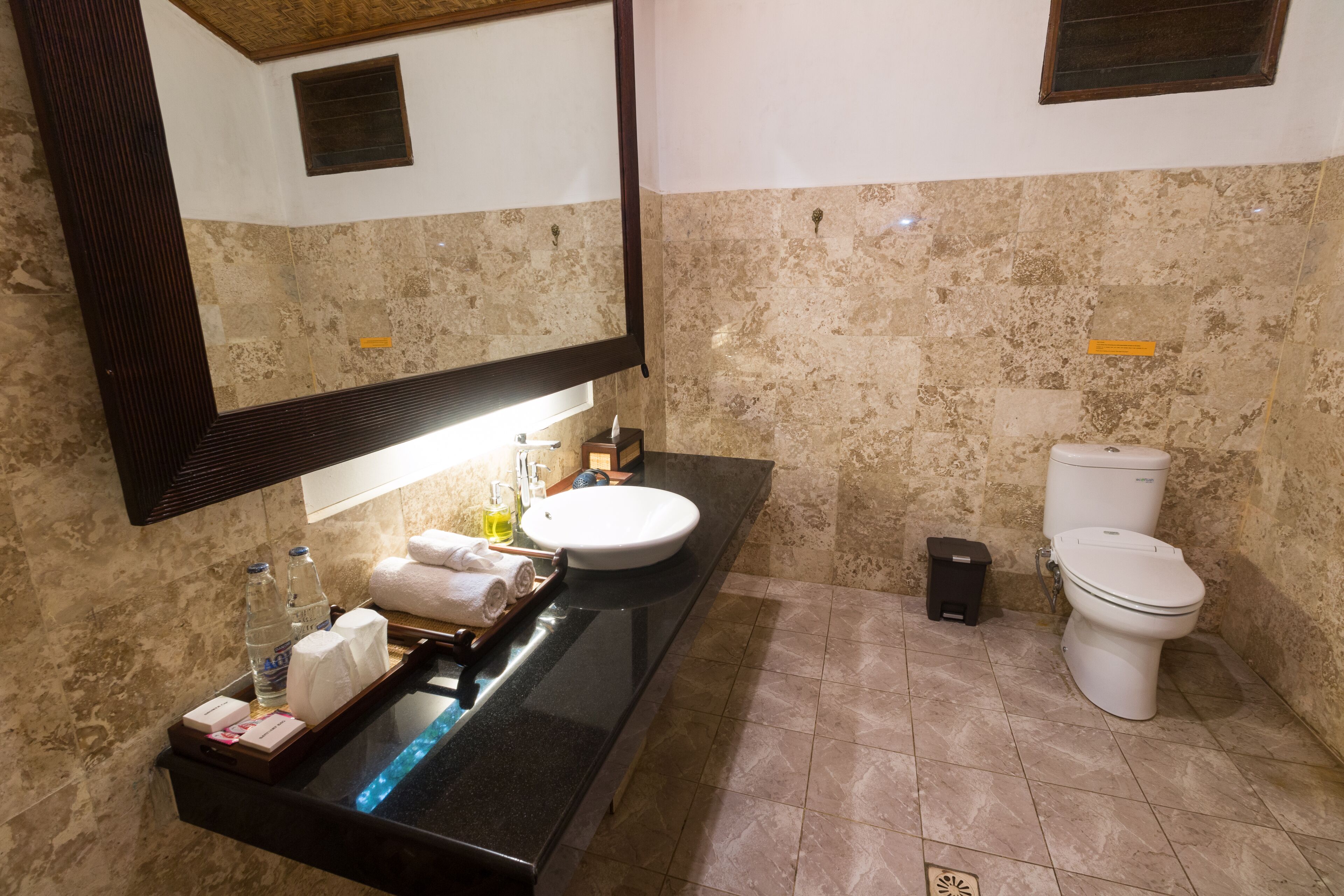 Un bagno con una parete in marmo, un lavabo con uno specchio, un water e un piccolo cestino.