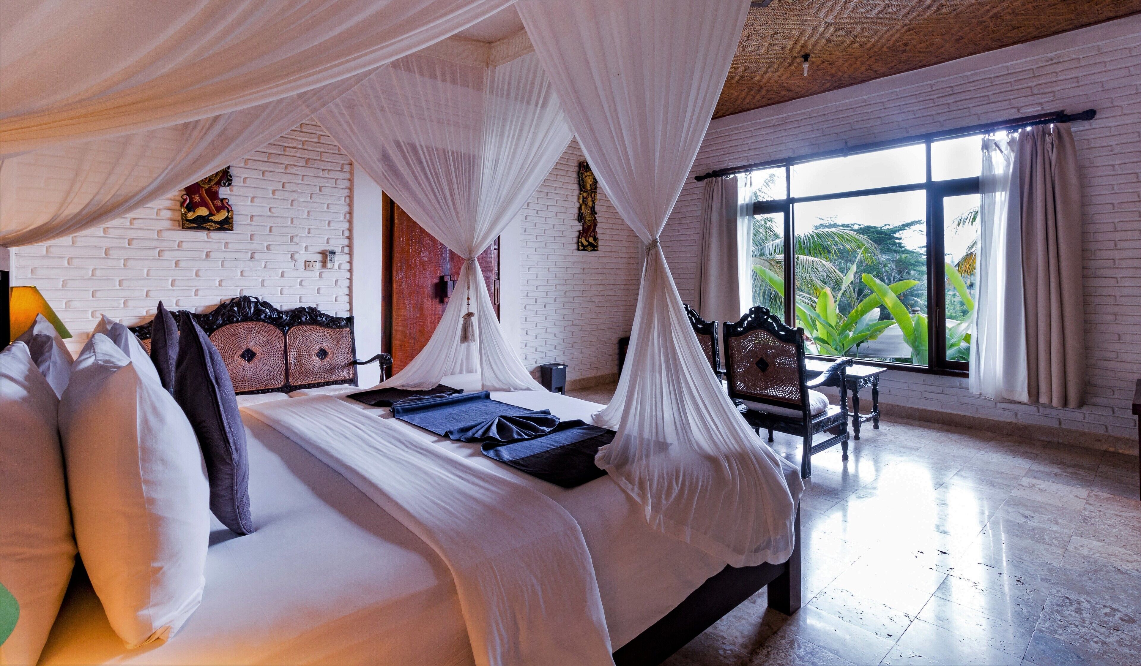 A spacious room with a large bed, a small table, and a view of greenery through the window.