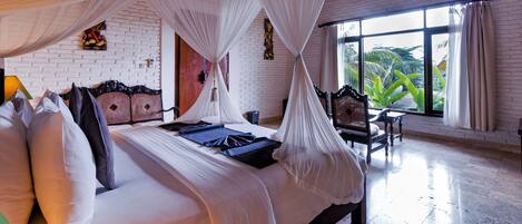 A spacious room with a large bed, a small table, and a view of greenery through the window.