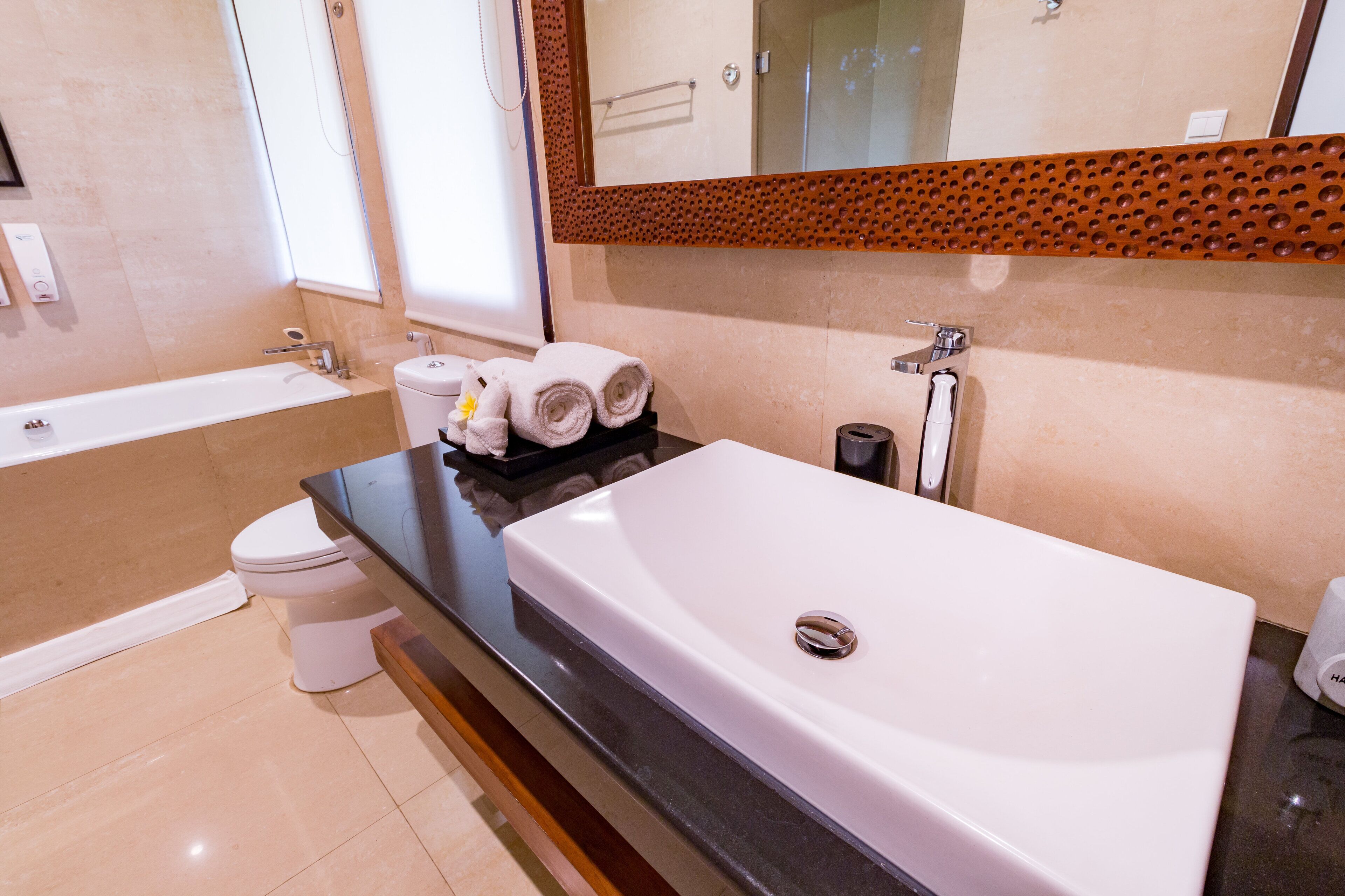 A modern bathroom with a large white bathtub, a separate toilet, and a vanity with a black countertop.