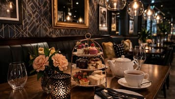 A dining table set with a tiered dessert stand, a teapot, cups, and a candle holder.