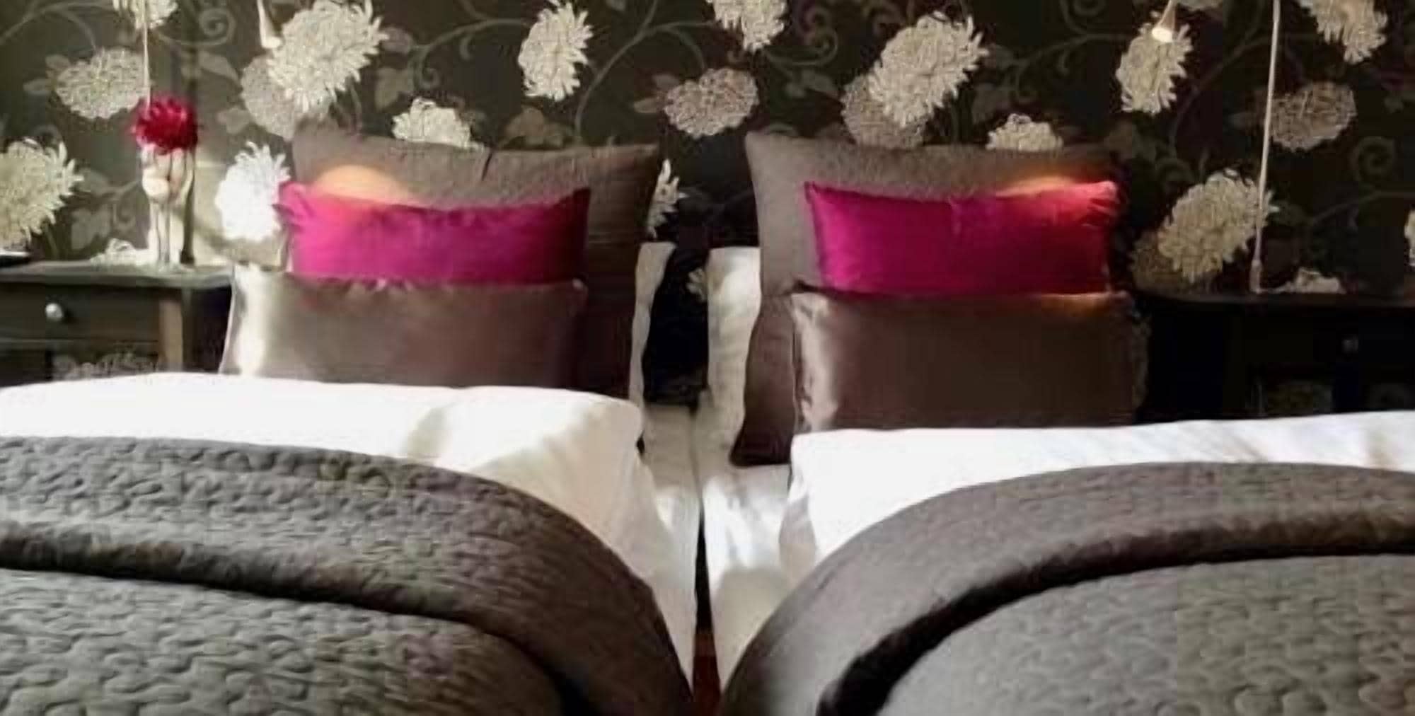 A double bed with a grey headboard and footboard, two pillows, and a nightstand with a vase of flowers.