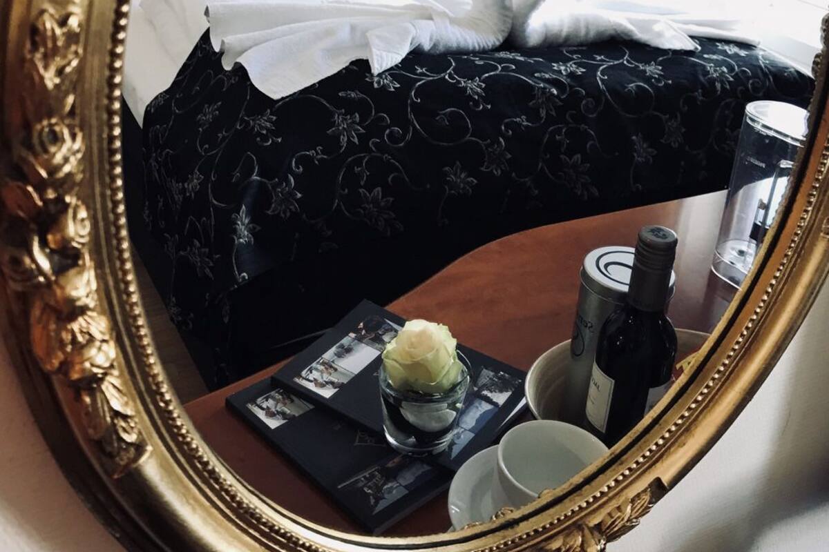 Habitación de hotel con cama, mesita de noche con una botella, una taza y un pequeño florero con una flor.