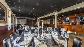 A restaurant with multiple tables set for dining, a bar area, and a well-lit interior.