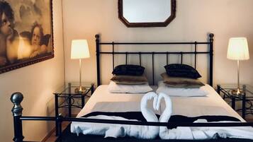 Una cama bien hecha con una toalla dispuesta en forma de corazón, dos lámparas de noche y una obra de arte enmarcada en la pared.