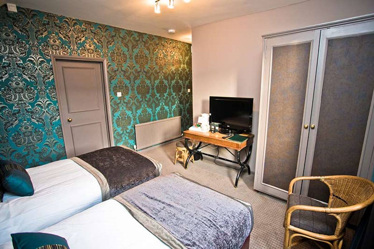 Habitación de hotel con dos camas, un escritorio con televisor, un armario y una silla de mimbre.