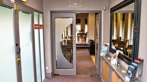 Pasillo de hotel con piso alfombrado, un mostrador de recepción con espejo y una puerta señalizada con 'EXIT'.