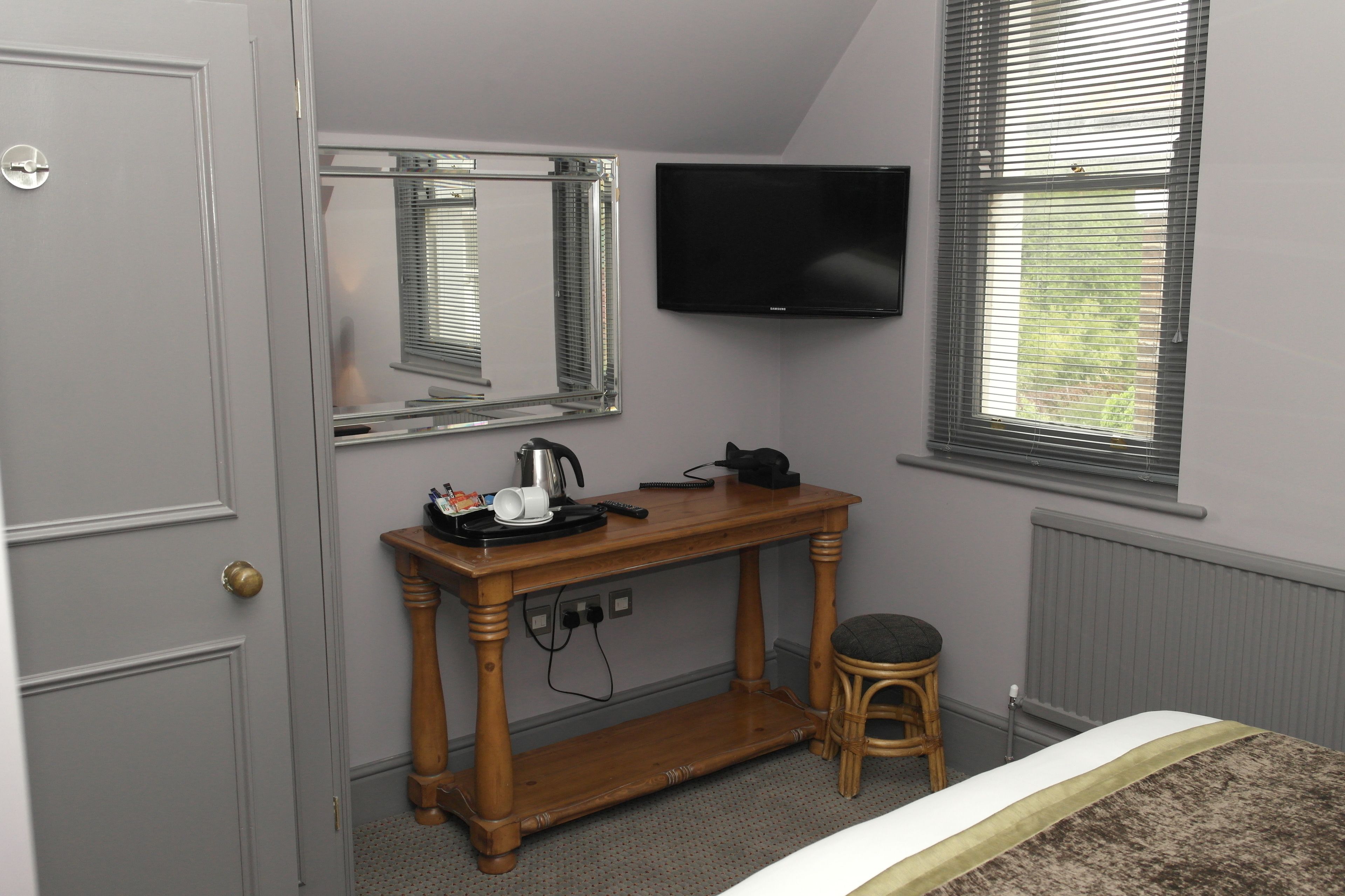 Une chambre à coucher avec un lit, un bureau en bois doté d’un miroir, une télévision et une fenêtre avec des stores.