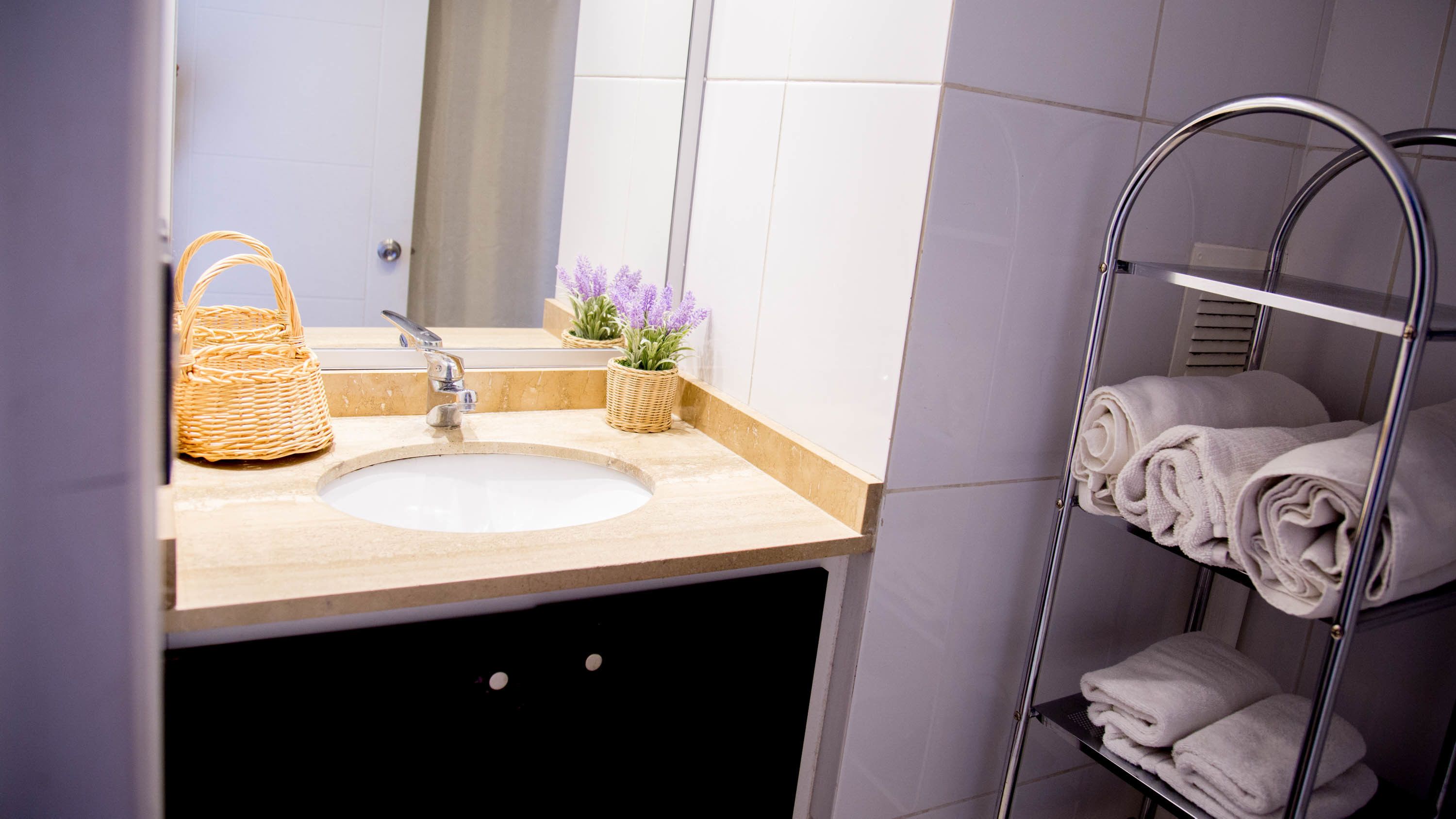 A bathroom with a sink, mirror, wicker basket, potted lavender, and a towel rack with folded towels.
