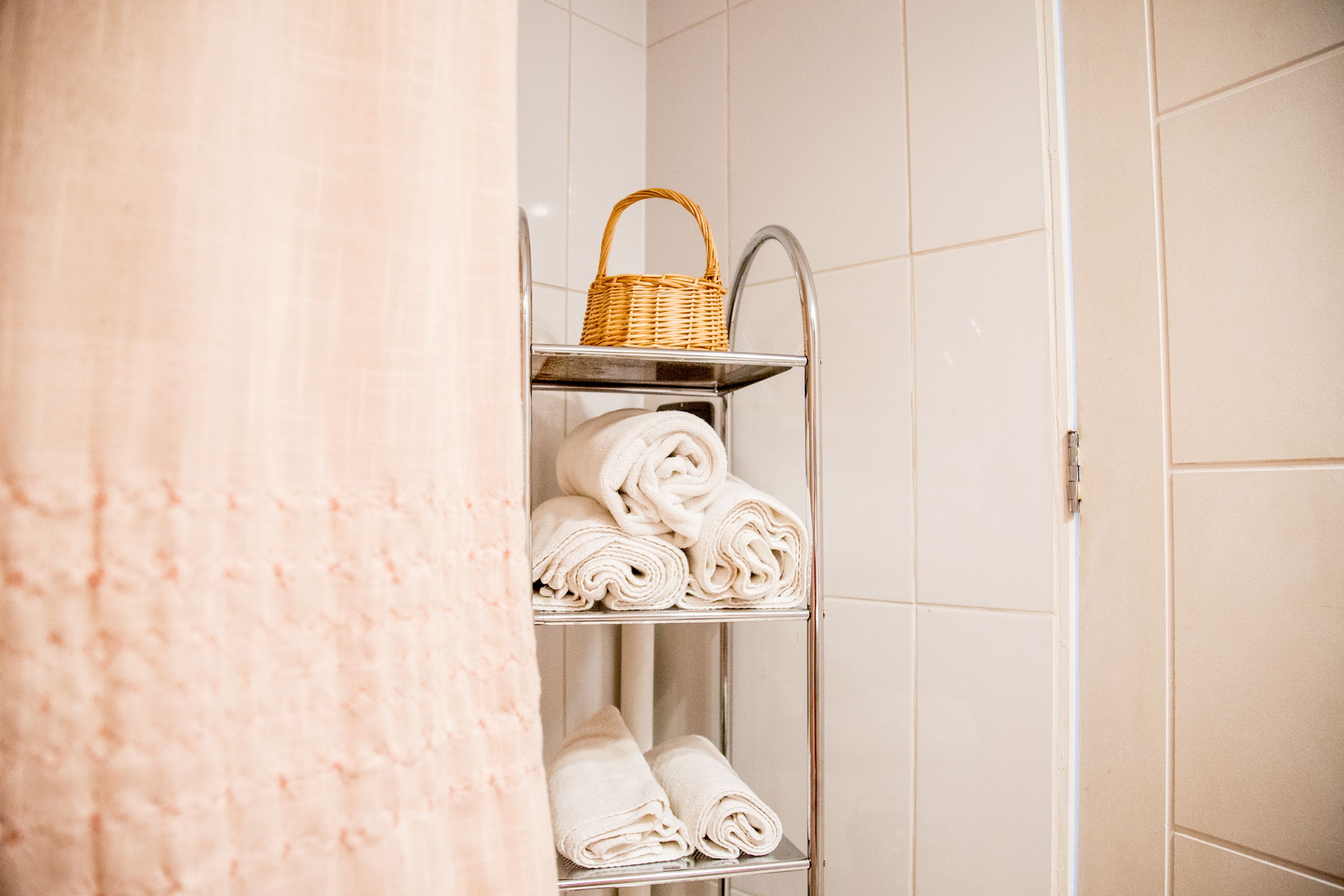 Un baño con un estante metálico que sostiene toallas enrolladas y una cesta de mimbre.