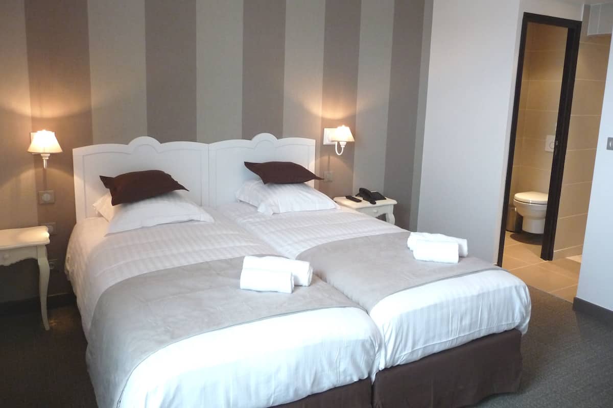 A double bed with white linens and two pillows, a bedside table with a lamp, and a telephone.