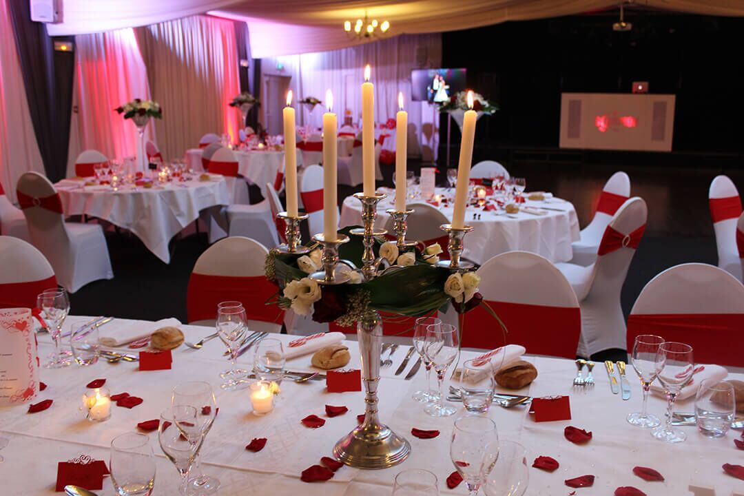 A banquet hall with round tables, white tablecloths, and red sashes on chairs.