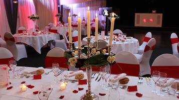 A banquet hall with round tables, white tablecloths, and red sashes on chairs.