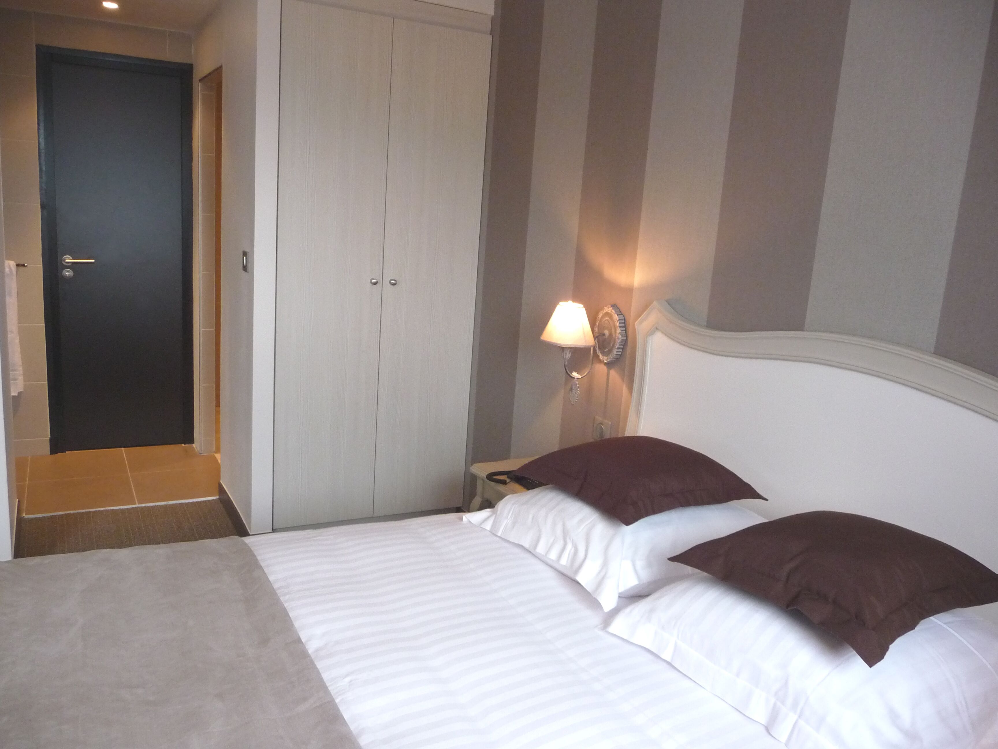Una habitación de hotel con cama, mesita de noche, lámpara y puerta.