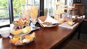 Een buffet met diverse gerechten, waaronder fruit, gebak en brood, gepresenteerd op een houten tafel met uitzicht op groen.