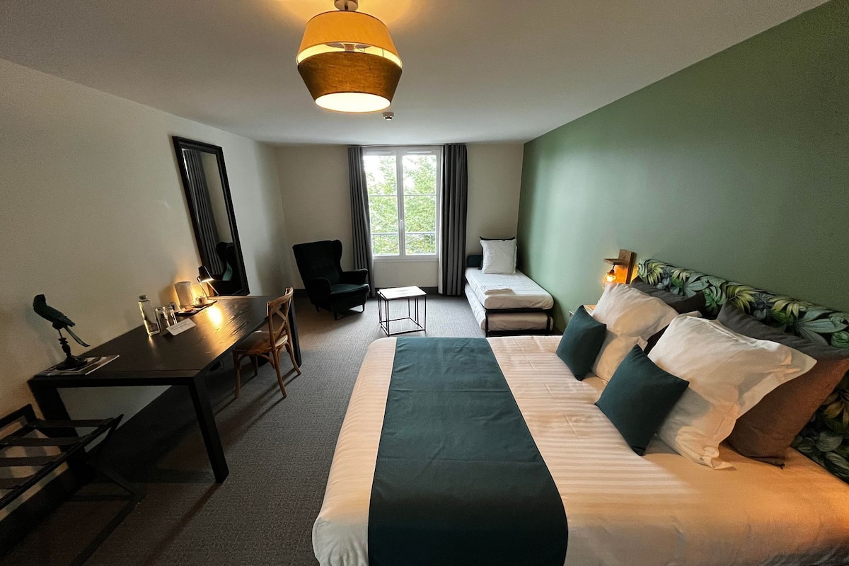 A hotel room with a bed, a desk, a chair, a small table, and a window with curtains.