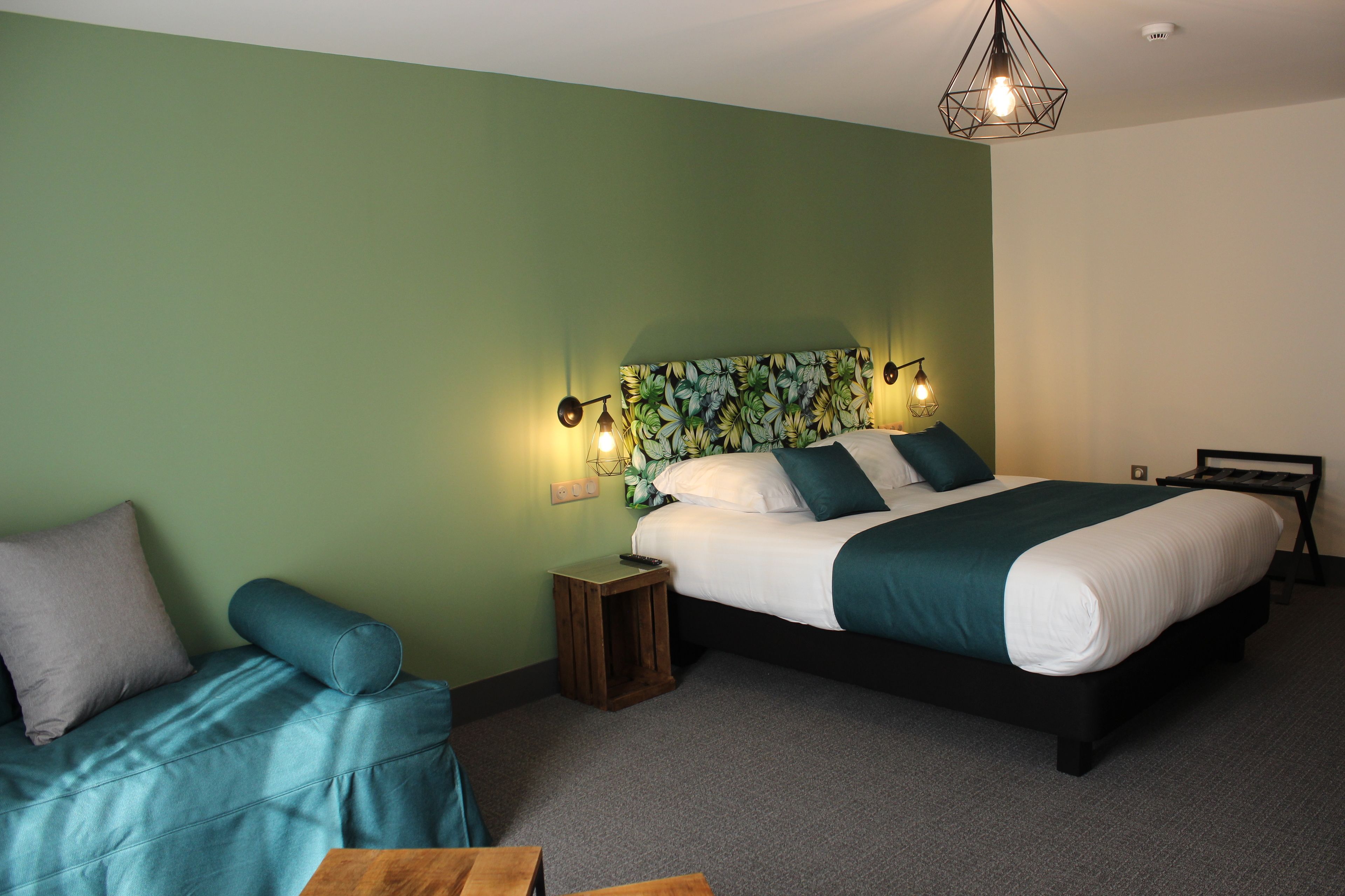 A bedroom with a bed, a sofa, a nightstand, and a hanging light fixture.
