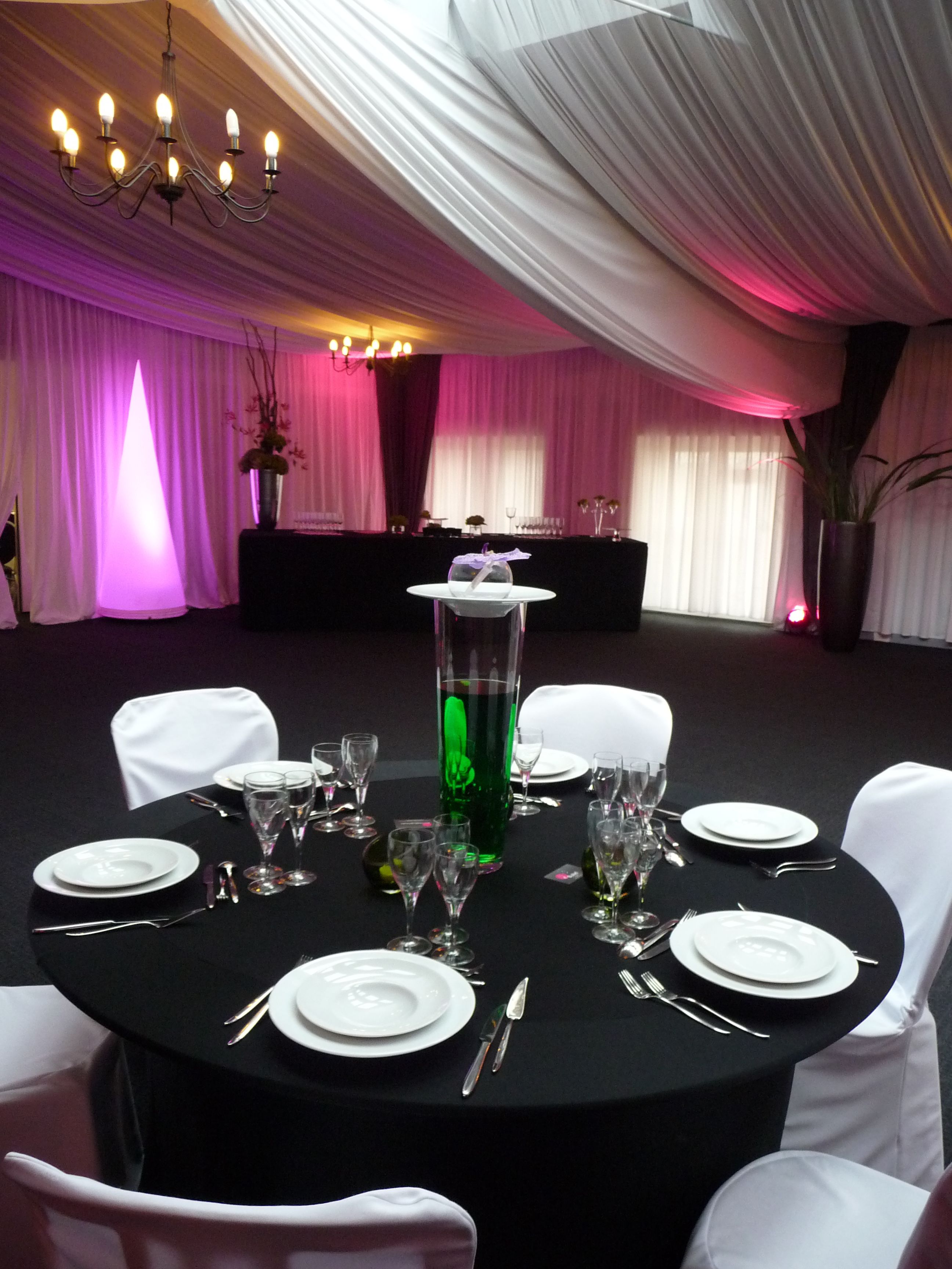 Un salón de banquetes con mesas redondas dispuestas para cenar, con manteles blancos, cubertería y copas de cristal.