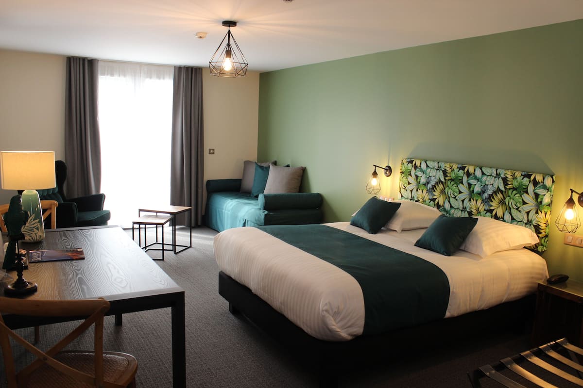 A hotel room with a bed, a desk, a chair, a lamp, and a window with curtains.