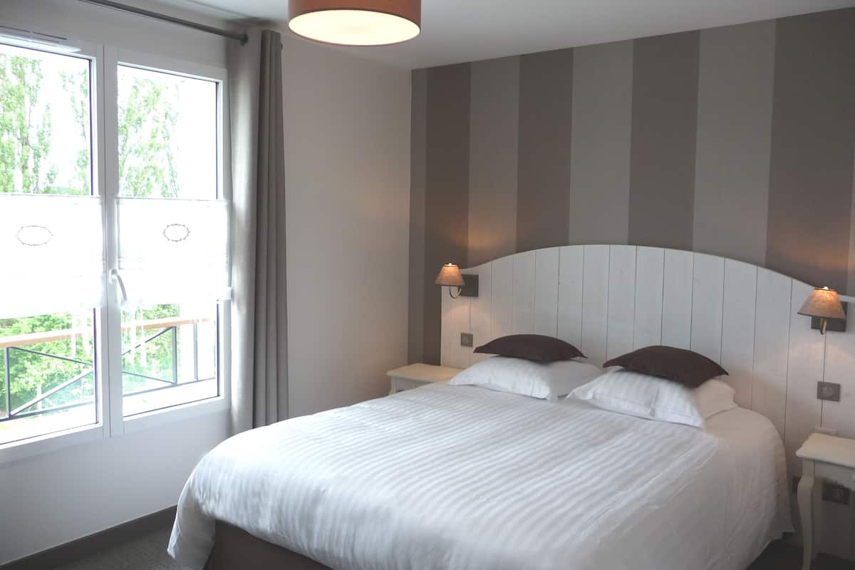 A hotel room with a large bed, two bedside tables, a headboard, and a window with curtains.