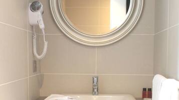 Une salle de bain équipée d’un miroir rond, d’un sèche-cheveux, d’un lavabo et d’une poubelle.