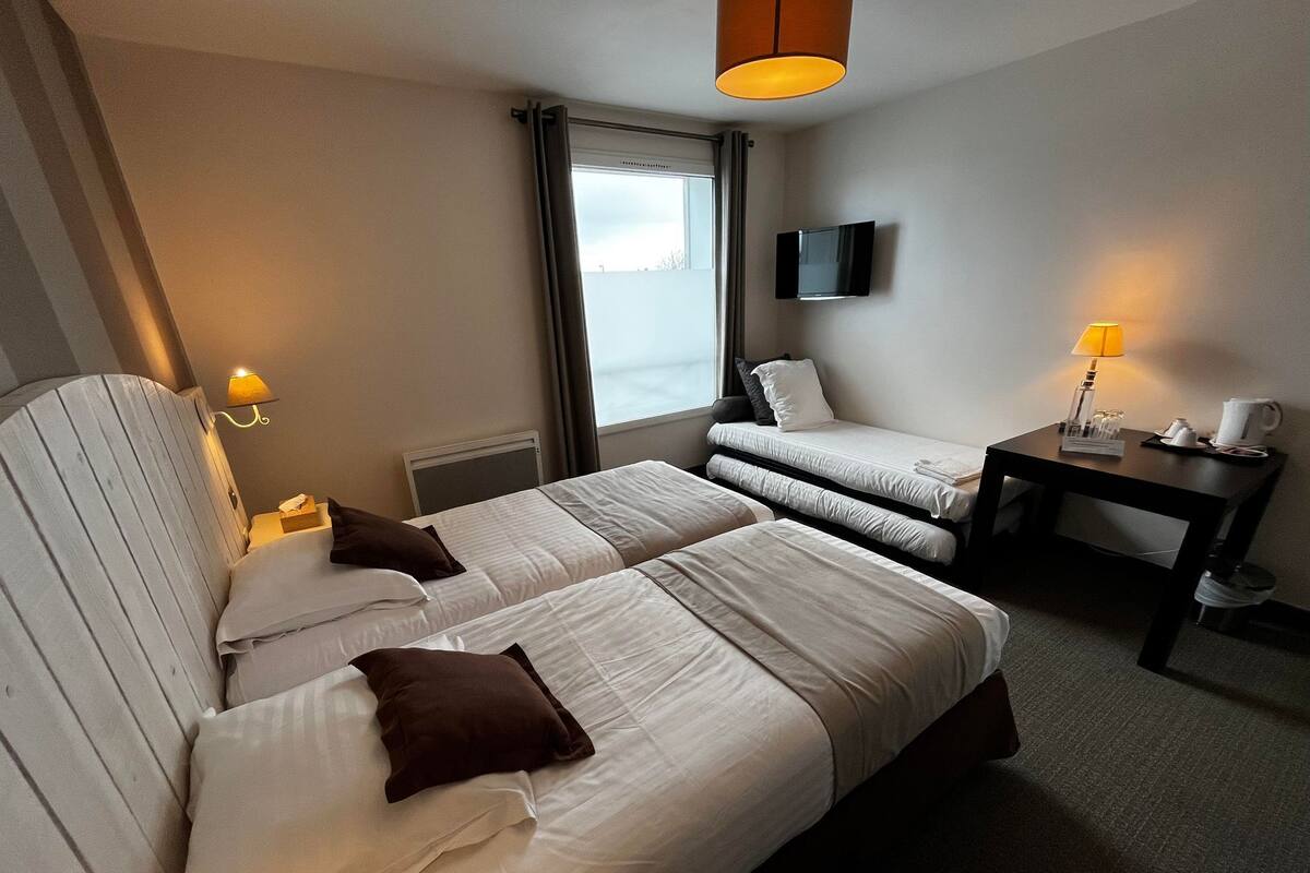 A hotel room with two beds, a TV, a desk with a lamp, and a window with curtains.