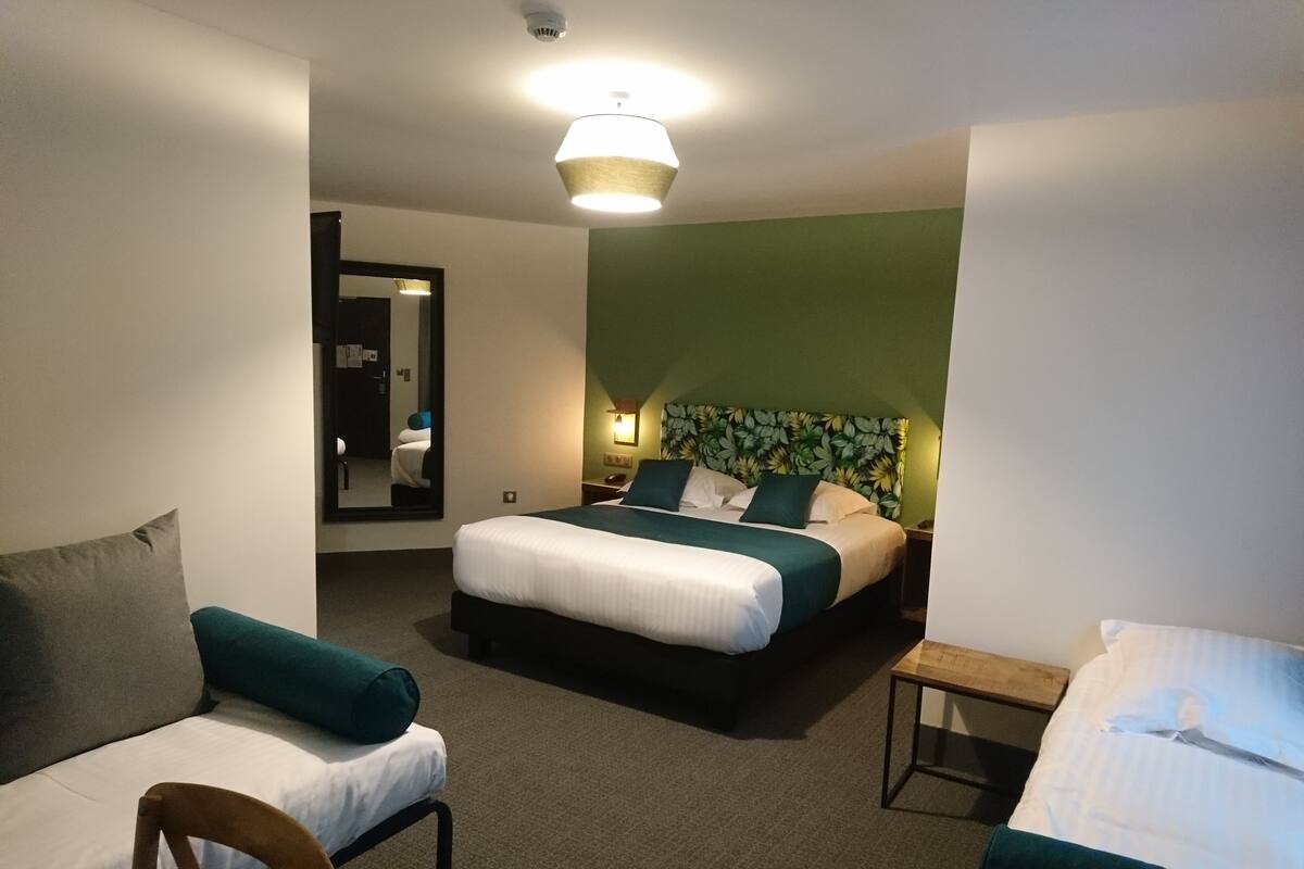 A hotel room with a large bed, a smaller bed, a sofa, and a desk.