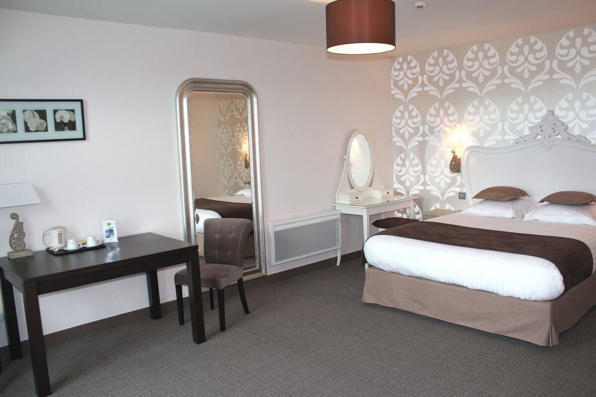 A hotel room with a bed, a desk, a chair, a mirror, and a lamp.