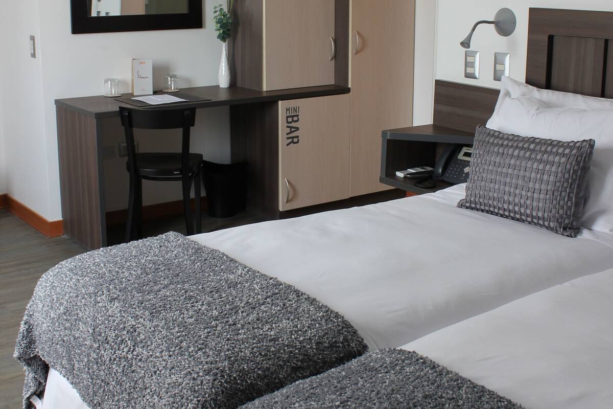A hotel room with a bed, a desk, a chair, a wardrobe, and a mirror.