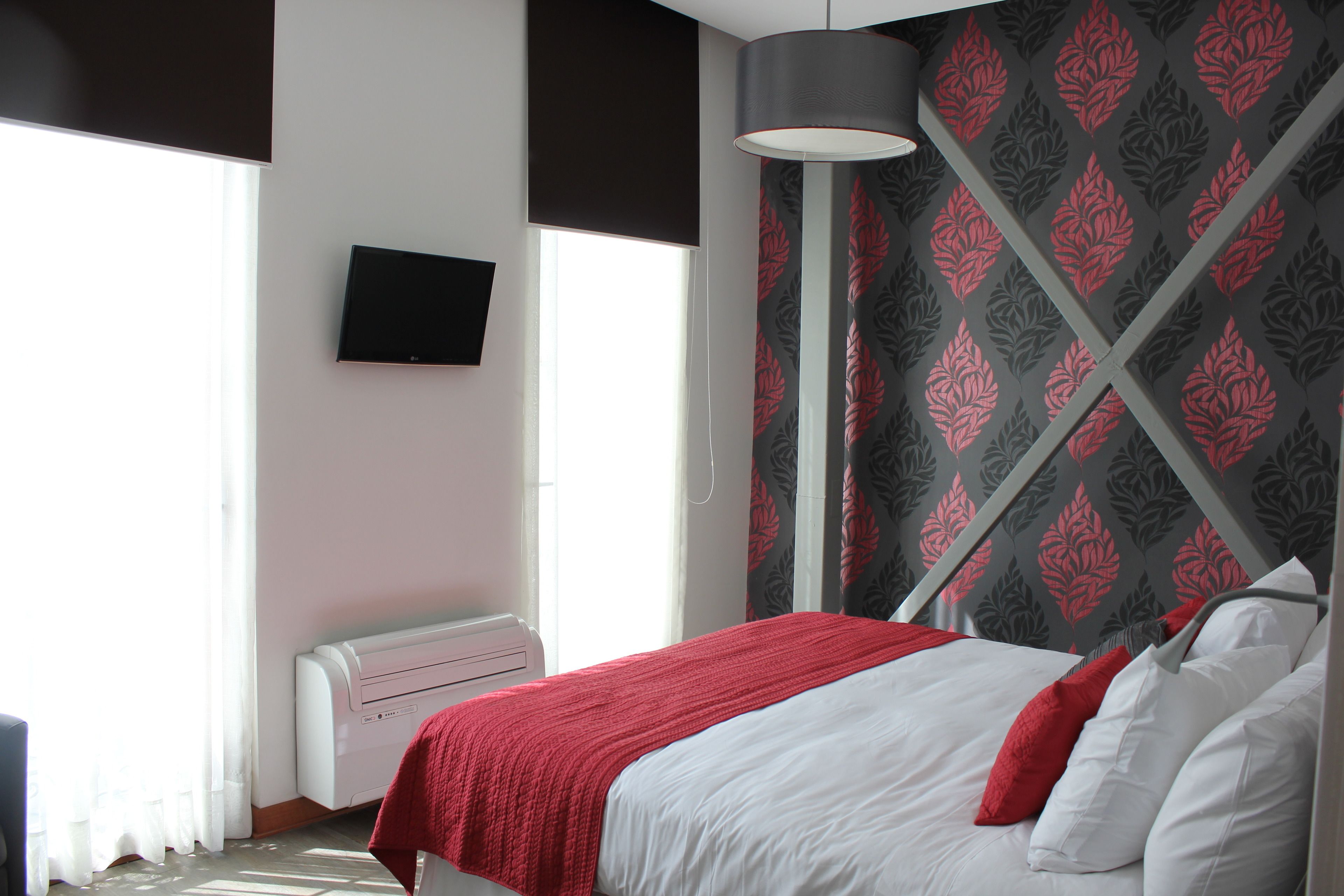 A bedroom with a bed, a flat-screen TV, and a window with curtains.