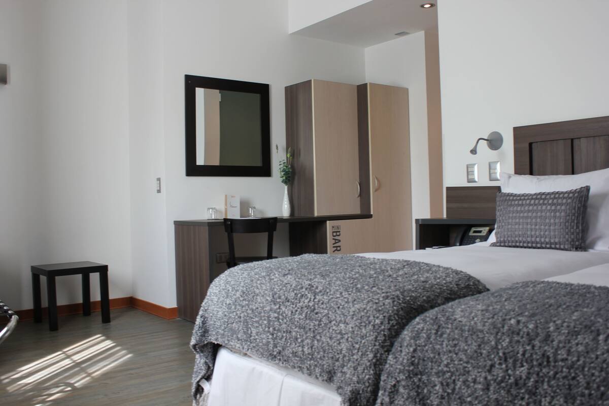 A hotel room with two beds, a wardrobe, a desk, and a mirror.