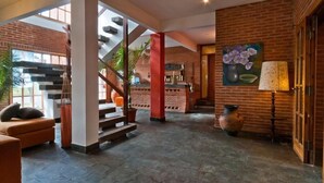Un hall d’entrée spacieux avec un escalier, un coin salon et un mur en briques orné d’un tableau.
