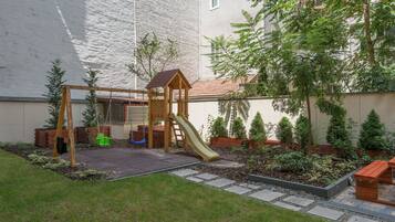 Explore the outdoor play area with a swing set, slide, and climbing structure amidst a beautifully manicured lawn and lush greenery.