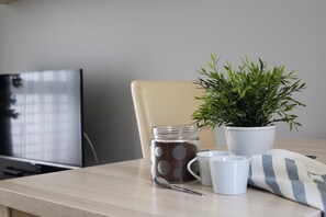 Una mesa con una planta en maceta, un tarro, una cuchara y dos tazas.
