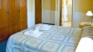 Habitación de hotel con cama, armario y baño visible a través de una puerta abierta.