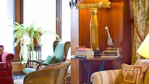 Una habitación acogedora con sillas de mimbre, un sofá a rayas y una mesa con libros y una lámpara.
