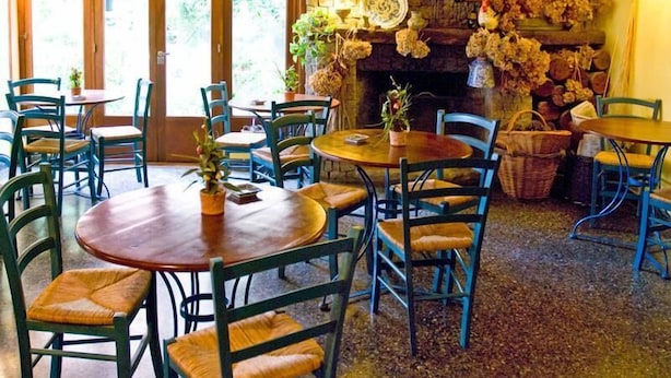 Un restaurante acogedor con mesas y sillas de madera, una chimenea de piedra y vistas al exterior.