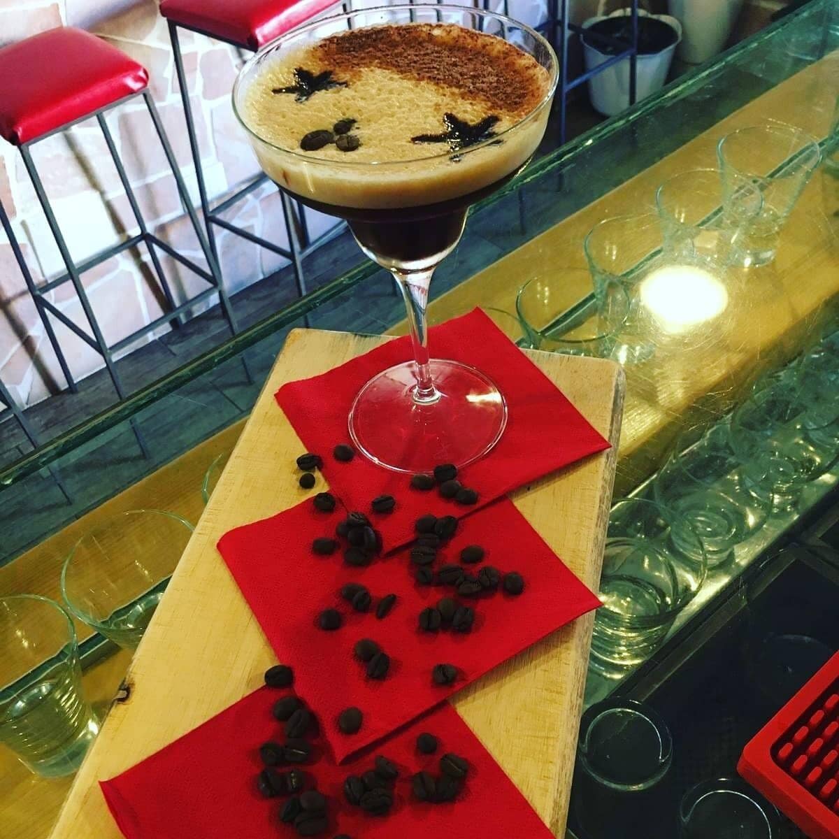 A martini glass with a frothy top, placed on a red napkin on a bar counter.