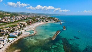 Un pueblo costero con una playa, aguas azul cristalino y un promontorio rocoso.