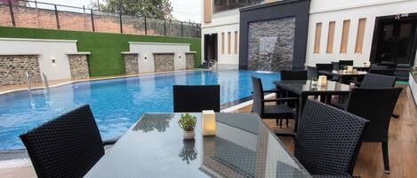 A poolside area with a glass table, black wicker chairs, and a stone wall.