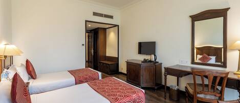 A hotel room with two beds, a desk, a chair, a television, and a mirror.