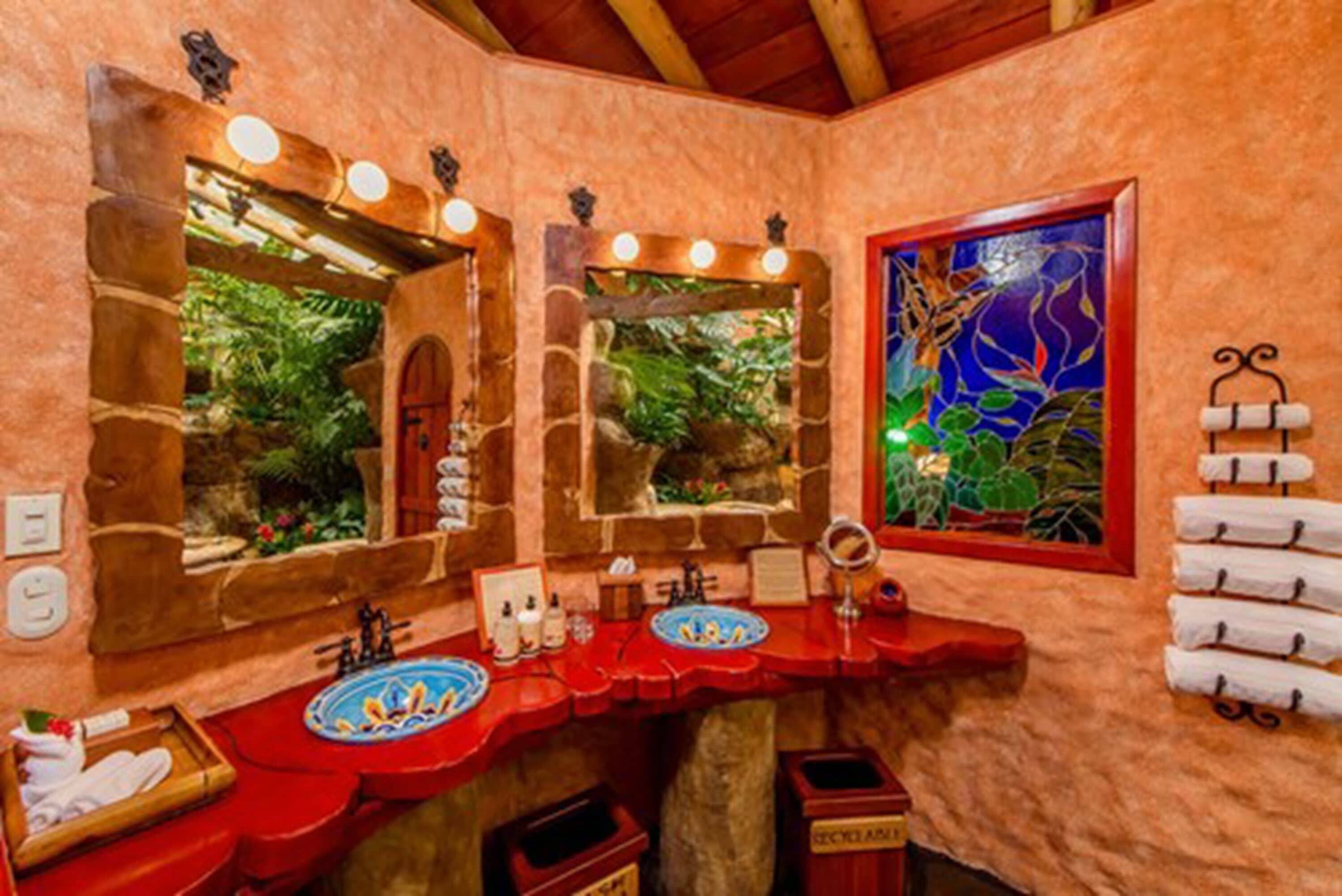 Un baño con un arco de piedra, dos lavamanos con encimeras rojas y un espejo grande.