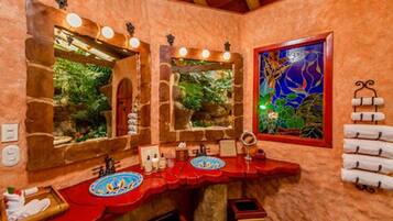 Un baño con un arco de piedra, dos lavamanos con encimeras rojas y un espejo grande.