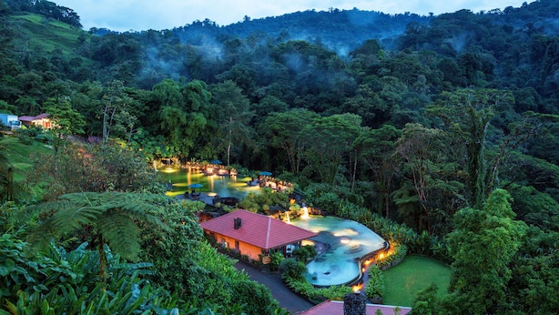A resort with a swimming pool, surrounded by lush greenery and hills.