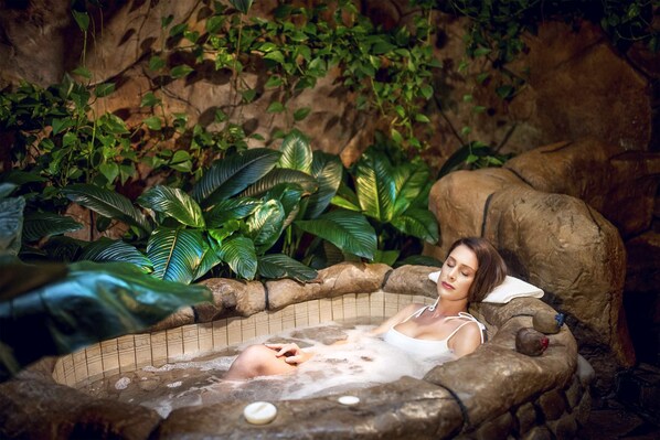 Una mujer relajándose en un jacuzzi rodeado de abundante follaje y rocas.