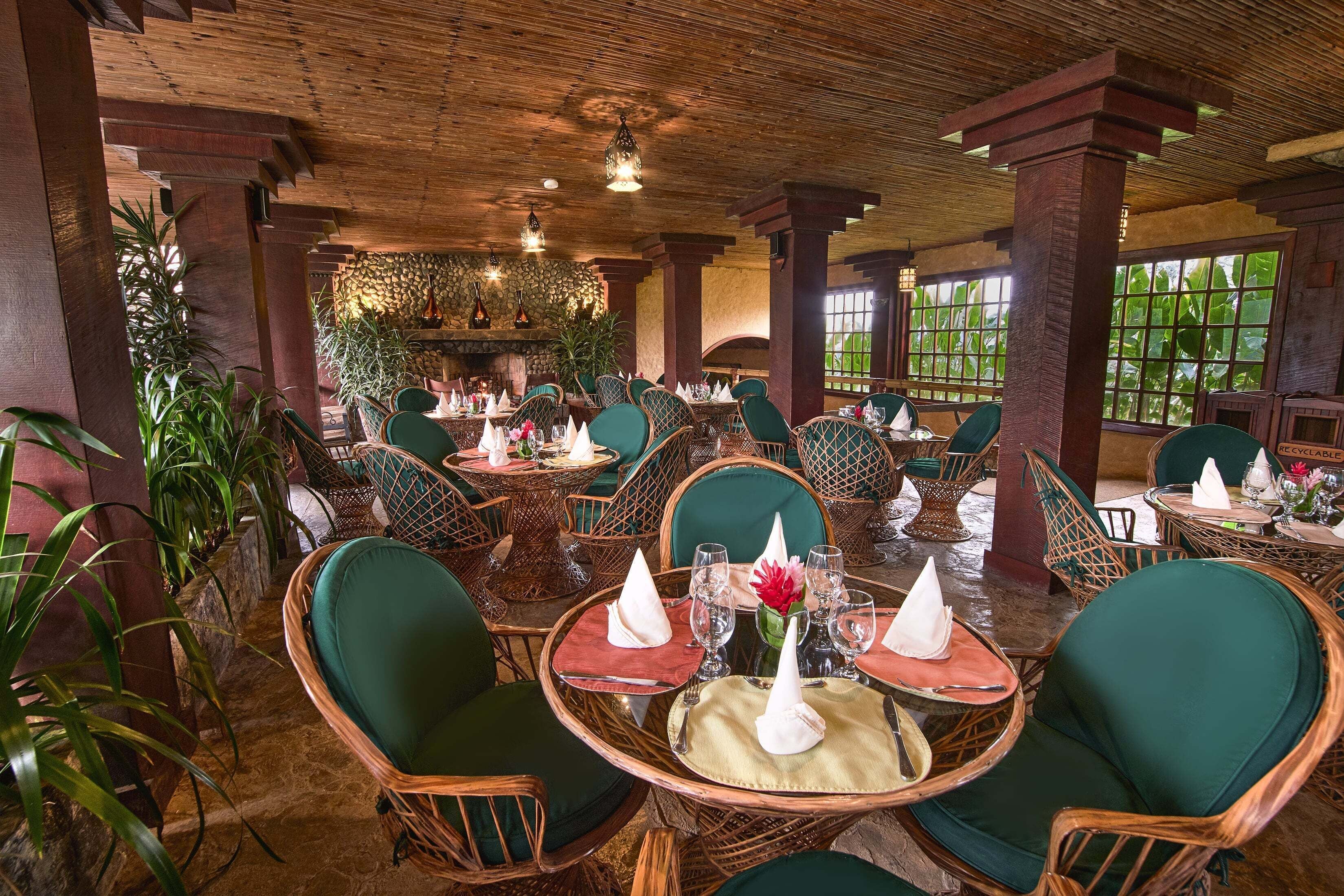 Un restaurante con mesas redondas, sillas con cojines verdes y techo de madera.