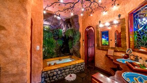 A bathroom with a stone bathtub, a wooden bench, and a mirror.