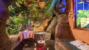 A cozy indoor garden with a stone fountain, a table with flowers, and a bench.